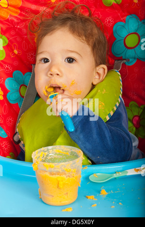 Baby boy mangiare le verdure purea da te stesso e seduti in poltrona Foto Stock