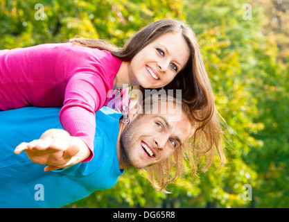 Felice coppia giovane piggybacking, braccia tese, sorridente. Foto Stock