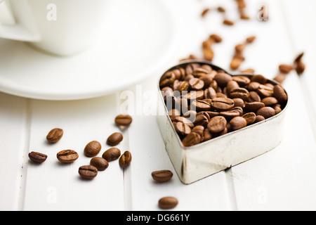 I chicchi di caffè in forma di cuore su bianco tavolo in legno Foto Stock