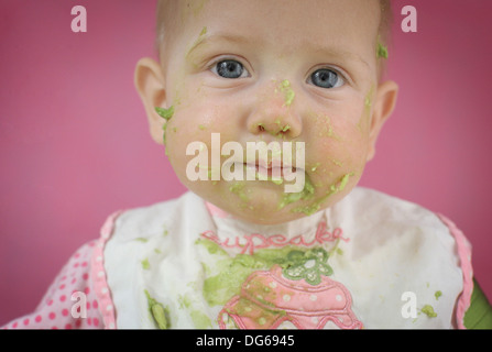 Baby ragazza sedeva in una alta sedia hi mangiare avocado Foto Stock