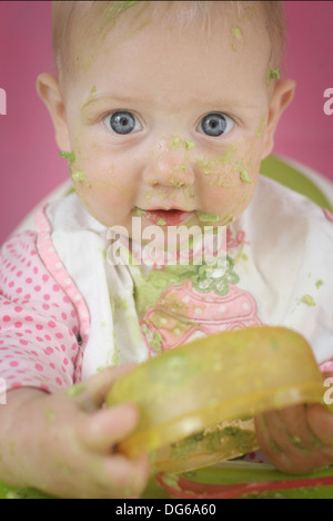 Baby ragazza sedeva in una alta sedia hi mangiare avocado Foto Stock