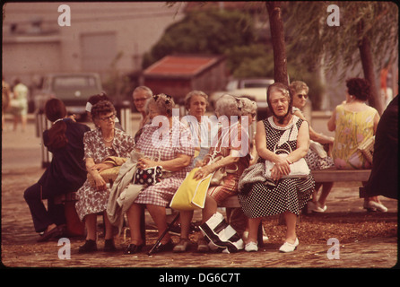 Due persone fanno una pausa e chiacchierano sedute sulla panchina del parco, catturando un momento di relax e interazione sociale. Foto Stock