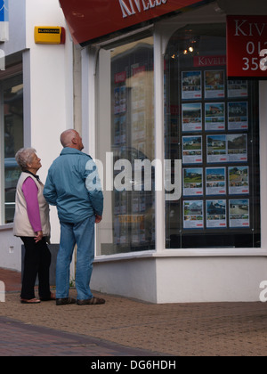 Vecchia coppia cercando in agente immobiliare della finestra, Bude, Cornwall, Regno Unito Foto Stock