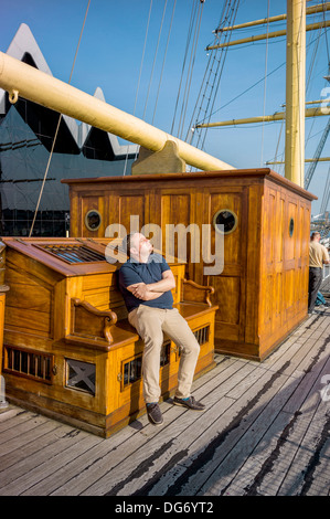 Un maschio adulto di catture la possibilità di prendere un po' di fine stagione sun su un vecchio legno nave a vela ormeggiata fino a Glasgow Foto Stock