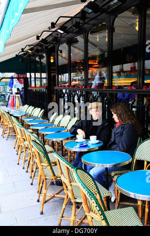 Due persone sedute a bere bevande calde e parlando in parte al di fuori del tradizionale café parigini nel periodo invernale Foto Stock