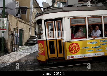 Alfama: un tram caricato con i turisti e con alcuni sardina-stile annuncio sul lato attraversando Alfama a Lisbona Foto Stock