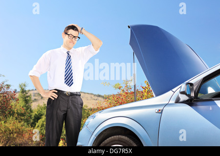 Giovane uomo in piedi vicino a Broken auto e pensando cosa fare Foto Stock