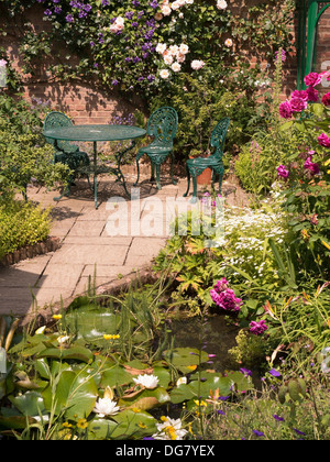 Attraente soleggiato giardino pavimentato patio con tavolo e sedie e un laghetto, Barnsdale Gardens, Oakham, Rutland, Inghilterra, Regno Unito. Foto Stock