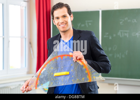 Insegnante o docente nella scuola in possesso di un triangolo geometria di fronte a una lavagna nella classe della scuola Foto Stock