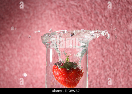 Fragola lasciato cadere in un bicchiere di acqua creando una splash Foto Stock