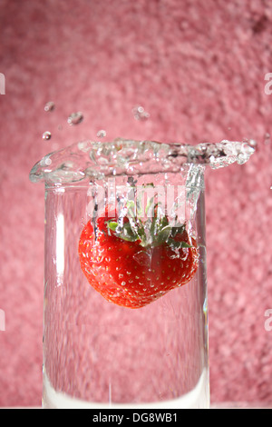 Fragola lasciato cadere in un bicchiere di acqua creando una splash Foto Stock