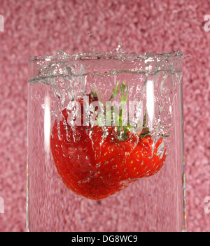 Fragola lasciato cadere in un bicchiere di acqua creando una splash Foto Stock