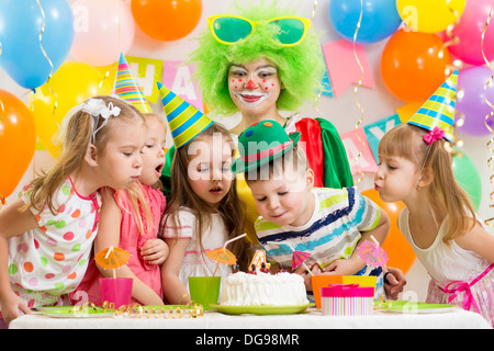 I bambini con clown celebrare la festa di compleanno e soffiando candela sulla torta Foto Stock