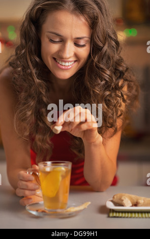 Sorridente giovane donna aggiungendo lo zucchero di canna nel cubo di tè allo zenzero Foto Stock