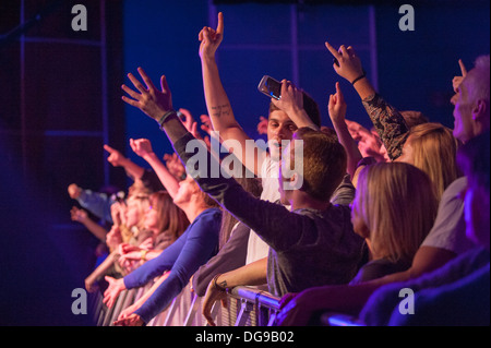 Giovani appassionati di musica in un concerto dal vivo schiacciato contro la barriera davanti al palco tifando, aggrappando e urlando in una band sul palco Foto Stock