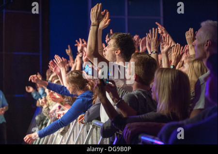 Giovani appassionati di musica in un concerto dal vivo schiacciato contro la barriera davanti al palco tifando, aggrappando e urlando in una band sul palco Foto Stock