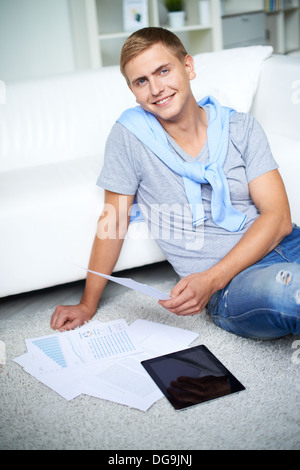 Immagine del giovane ragazzo in seduta informale sul pavimento e guardando la telecamera con un sorriso Foto Stock