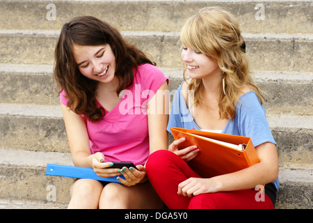 Due ragazze teenager ridere texto o internet sul loro telefono cellulare o cellulare Foto Stock