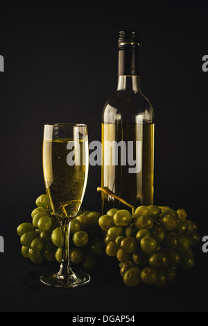 Il vino bianco in bottiglia e di vetro e uve bianche su sfondo scuro Foto Stock