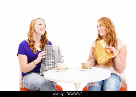 Felice redhead le donne sedute a un tavolo da caffè con le borse della spesa su sfondo bianco Foto Stock