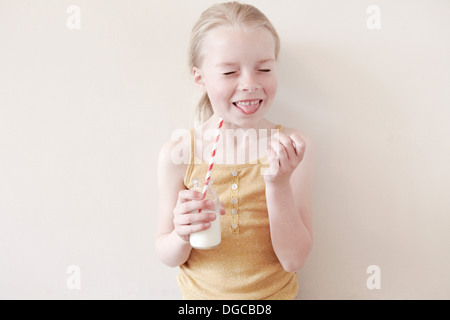 Ragazza giovane con la lingua fuori e tenendo un bicchiere di latte Foto Stock