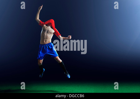 Maschio di giocatore di calcio celebrando con camicia sopra la testa Foto Stock