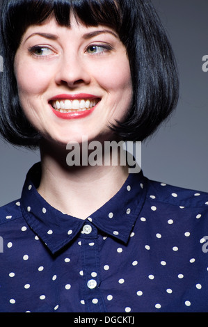 Giovane donna in blue spotted camicetta guardando lontano, sorridente Foto Stock