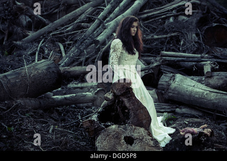 La donna in un antico edificio di abito da sposa davanti a tagliare gli alberi e creepy doll Foto Stock