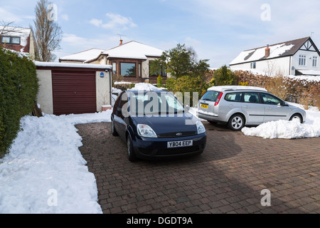 Auto parcheggiate su neve cancellata drive nella parte anteriore della casa Foto Stock