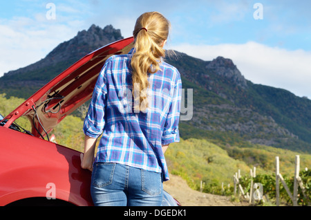 Giovane donna vicino a Broken auto richiede assistenza per guardare sotto il cofano aperto Foto Stock