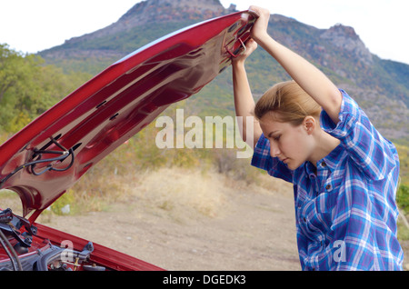 Giovane donna vicino a Broken auto richiede assistenza per guardare sotto il cofano aperto Foto Stock