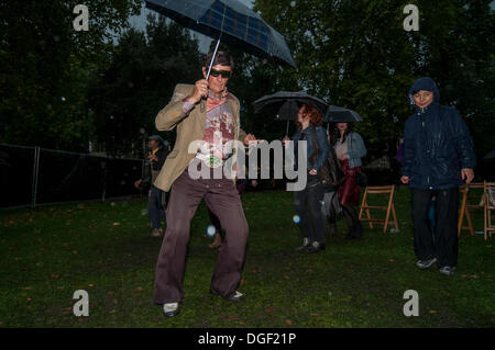 Russell Square, Bloomsbury, Londra, UK, 20 Ottobre 2013 - The Bloomsbury Festival 2013, un 'autunno festival di arte, di conoscenze e di Immaginazione' featured molti eventi eclettico per il pubblico di godere. Qui, un uomo in un costume colorato che impugnano un ombrello, conduce la danza, nella pioggia torrenziale, alla salsa cubana musica fornita dalla band di 'Sarabanda'. Credito: Stephen Chung/Alamy Live News Foto Stock