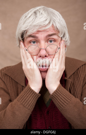 Scioccato, grigio capelli vecchio uomo, con entrambe le mani sul suo viso guardando dritto la fotocamera. Foto Stock