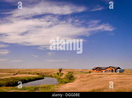 Una casa su una prateria da un lago sotto un vivid blue sky Foto Stock