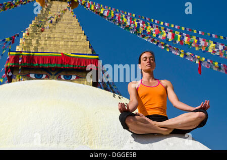 Giovane donna a praticare yoga a Boudnanath stupa, mostrando il Padmasana pongono o Lotus pongono, Valle di Kathmandu, Kathmandu Foto Stock