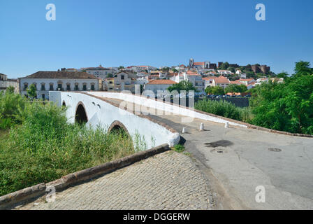 Un antico ponte in pietra che attraversa il Rio Arado fiume, di fronte al centro storico della città e il castello medievale di Castelo de Silves Foto Stock