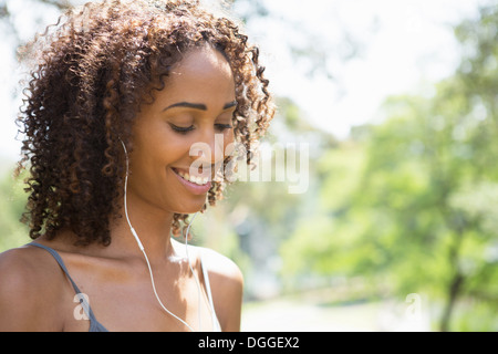 Metà donna adulta che indossa gli auricolari, sorridente Foto Stock
