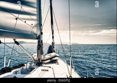 Skipper seduto a prua del suo yacht a vela guardando verso poppa, Mare Adriatico, Croazia, Europa Foto Stock