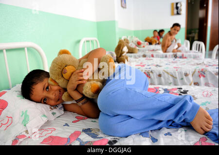 Ragazzo con un grosso orso di peluche sul suo letto nel dormitorio di un orfanotrofio, Queretaro, Messico, America del Nord e America Latina Foto Stock