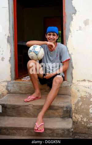 Adolescente con il calcio seduto davanti a casa sua in una favela, Poxoréo, Mato Grosso, Brasile Foto Stock