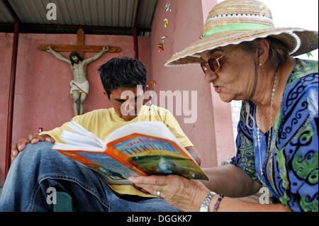 Donna anziana con cappello per il sole di insegnamento di una giovane migrante a leggere in un rifugio per i paesi dell'America Latina migranti, Ixtepec, Oaxaca, Messico Foto Stock