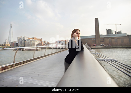 Donna sul cellulare sul Millennium Bridge, London, England, Regno Unito Foto Stock