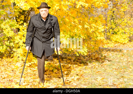 Anziani disabili amputato maschio in una caduta park con una passeggiata sulle sue stampelle Circondato da colorati in giallo le foglie di autunno Foto Stock