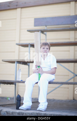 Ragazzo holding cricket bat seduti sulle gradinate Foto Stock
