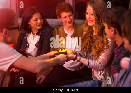 Gruppo di adolescenti seduti intorno a torta di compleanno Foto Stock