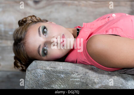 Giovane donna sorridente indossando una rosa top senza maniche giacente su una panca in legno, ritratto Foto Stock
