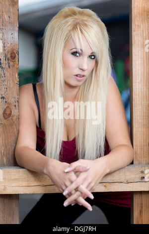 Giovane donna con capelli lunghi biondi che pongono tra un telaio di legno, ritratto Foto Stock