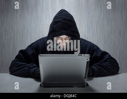 Un uomo incappucciato che rappresenta un cyber criminali. Foto Stock