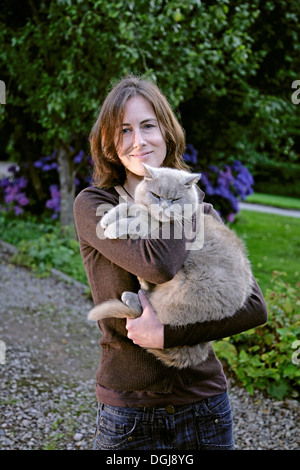 Giovane donna con un gatto grigio nelle sue braccia. Foto Stock