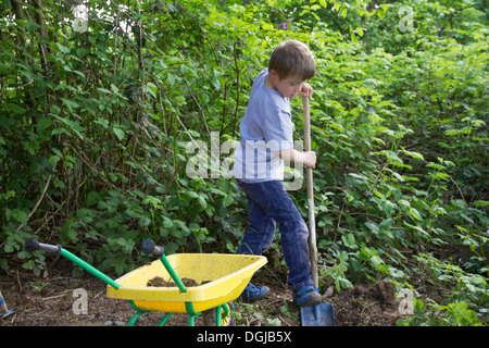 Ragazzo scavando nel giardino con spade giocattolo e la carriola Foto Stock